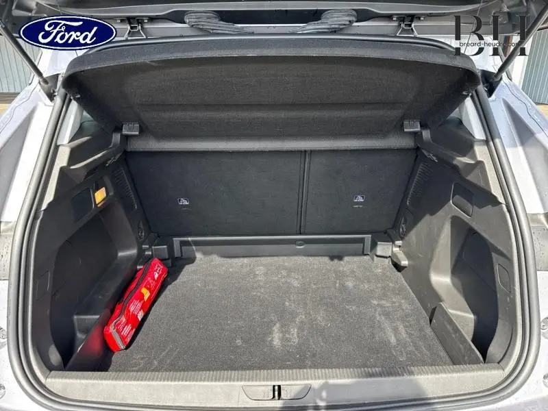 Coffre ouvert vu de l'arrière d'un Opel Grandland gris Kontrast Métallisé avec tapis noir et trousse de secours rouge.