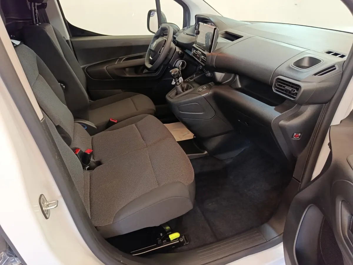 Intérieur côté conducteur du Peugeot Partner blanc 2025, montrant les sièges, tableau de bord et levier de vitesses manuel.