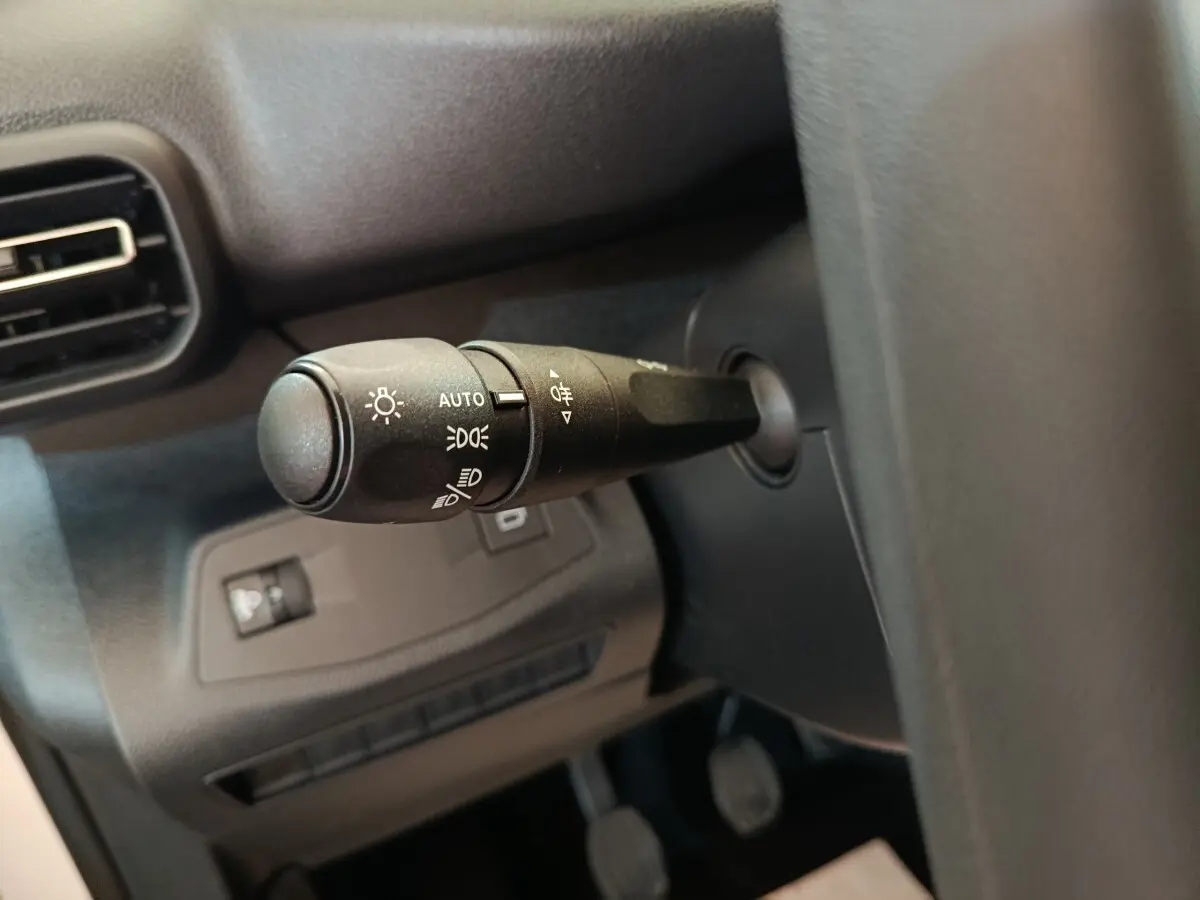 Gros plan sur la commande des phares à gauche du volant dans l’habitacle sombre d’un Peugeot Partner blanc.