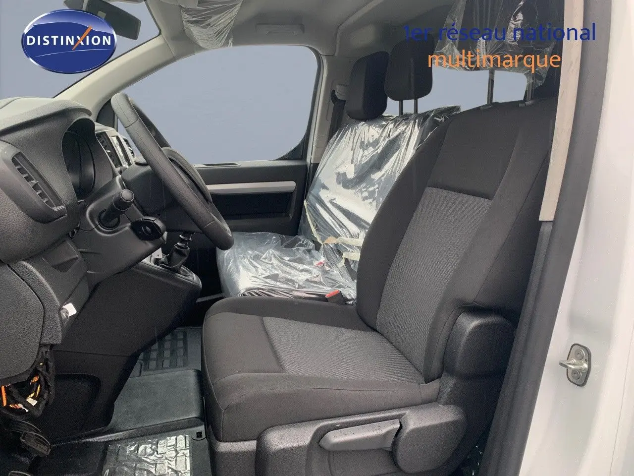 Vue intérieure côté conducteur du Peugeot Expert Long 2023, sièges noirs avec protection plastique sur la banquette passager.