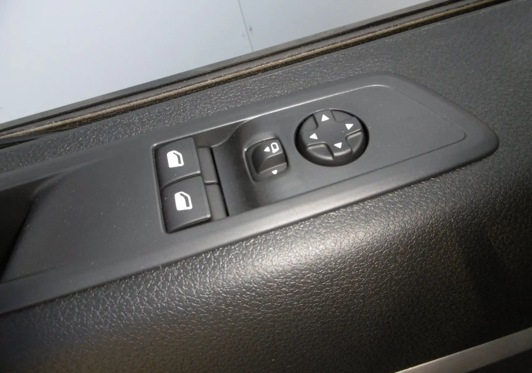 Gros plan sur les commandes de réglage des rétroviseurs et des vitres électriques sur la portière noire intérieure du Peugeot Expert Long blanc.