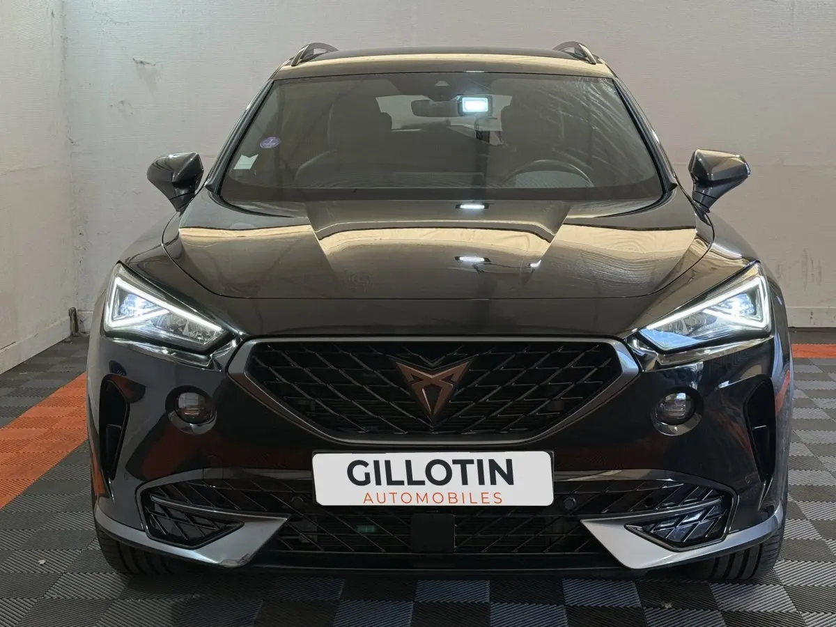 Vue frontale d'un CUPRA Formentor noir 2023 avec phares LED allumés et calandre distinctive au logo cuivre.