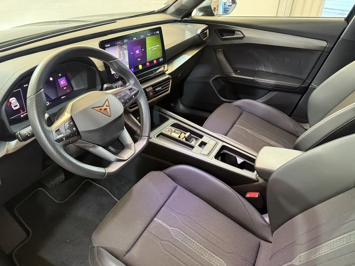 Intérieur du CUPRA Formentor noir 2023, vue côté conducteur, volant cuir, écran tactile central et sièges tissu gris.