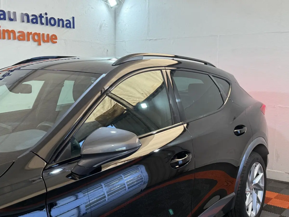 Profil côté gauche d'un CUPRA Formentor noir brillant avec rétroviseur et barres de toit visibles en intérieur showroom.