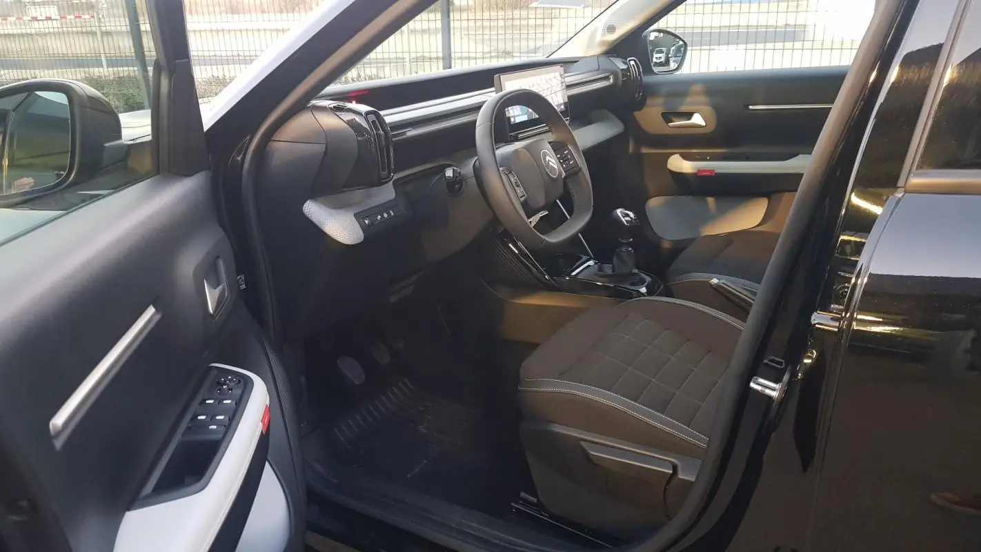 Intérieur avant gauche d’une Citroën C3 noire 2025, montrant le tableau de bord et les sièges tissu foncé.
