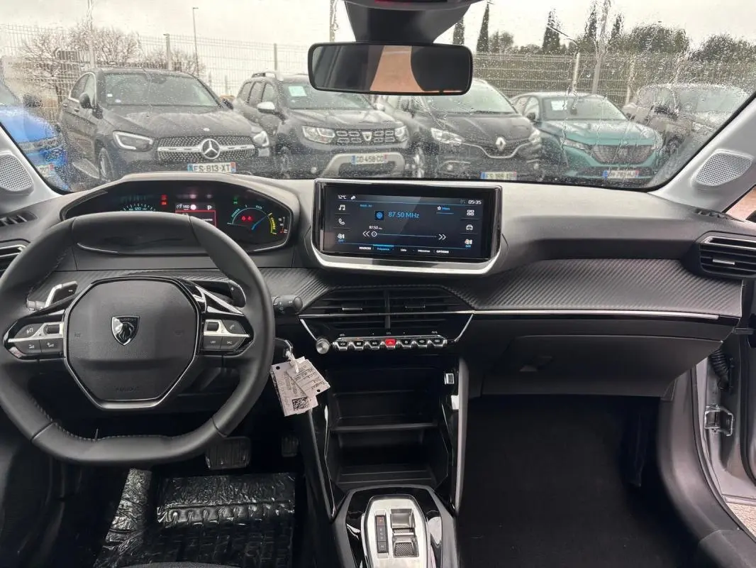 Vue intérieure avant de la Peugeot 208 Hybrid gris, avec volant multifonction, écran tactile et cockpit numérique.