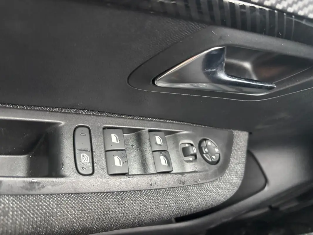 Gros plan sur les commandes des vitres électriques et rétroviseurs sur la porte intérieure côté conducteur d'une Peugeot 208 gris hybride.