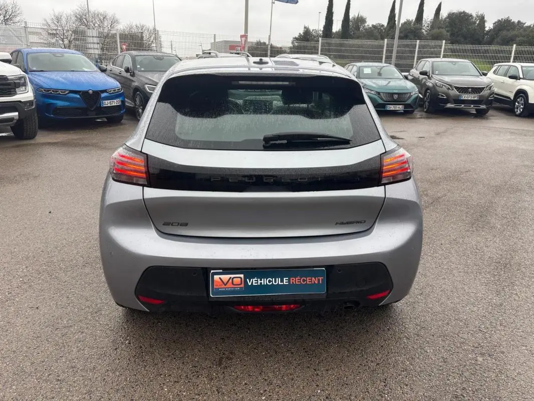 Vue arrière d’une Peugeot 208 Hybrid gris 2025 avec feux LED allumés et logo distinctif sur un parking.