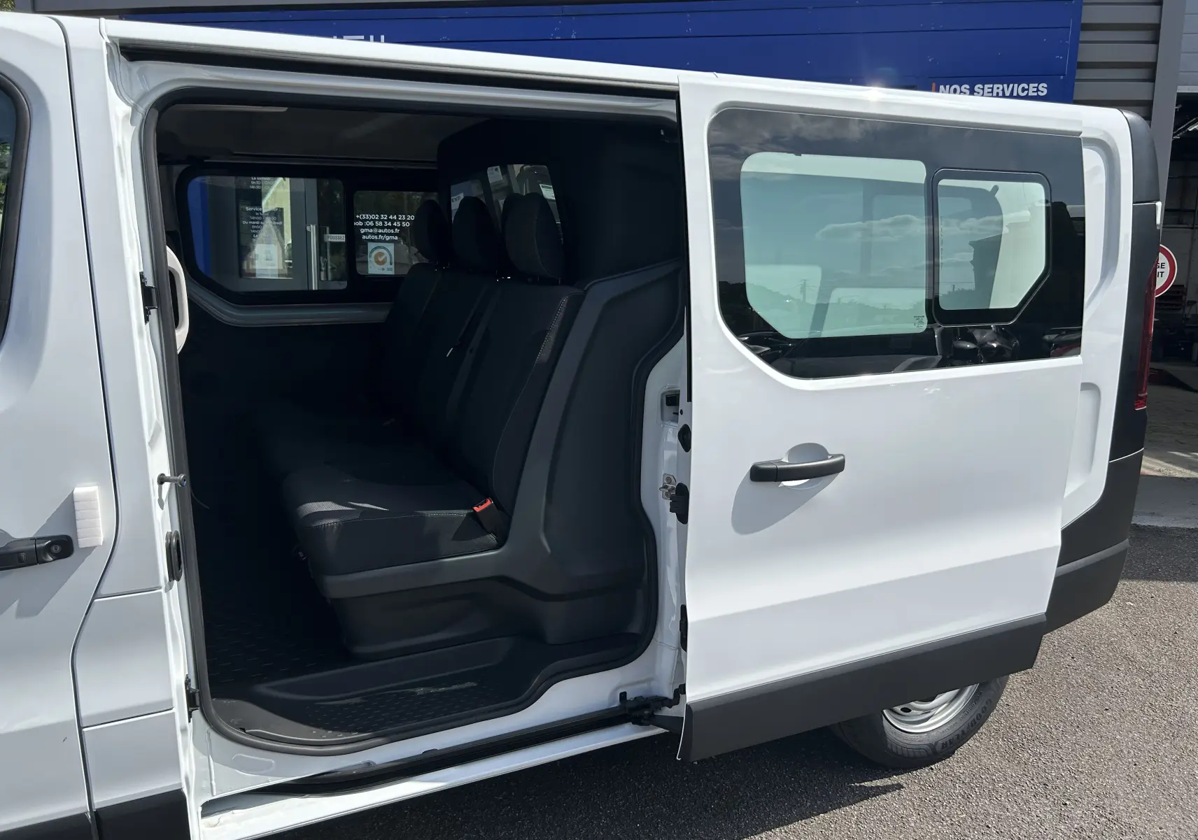 Vue latérale droite d’un Renault Trafic cabine approfondie blanc avec porte coulissante ouverte montrant la banquette arrière 3 places.