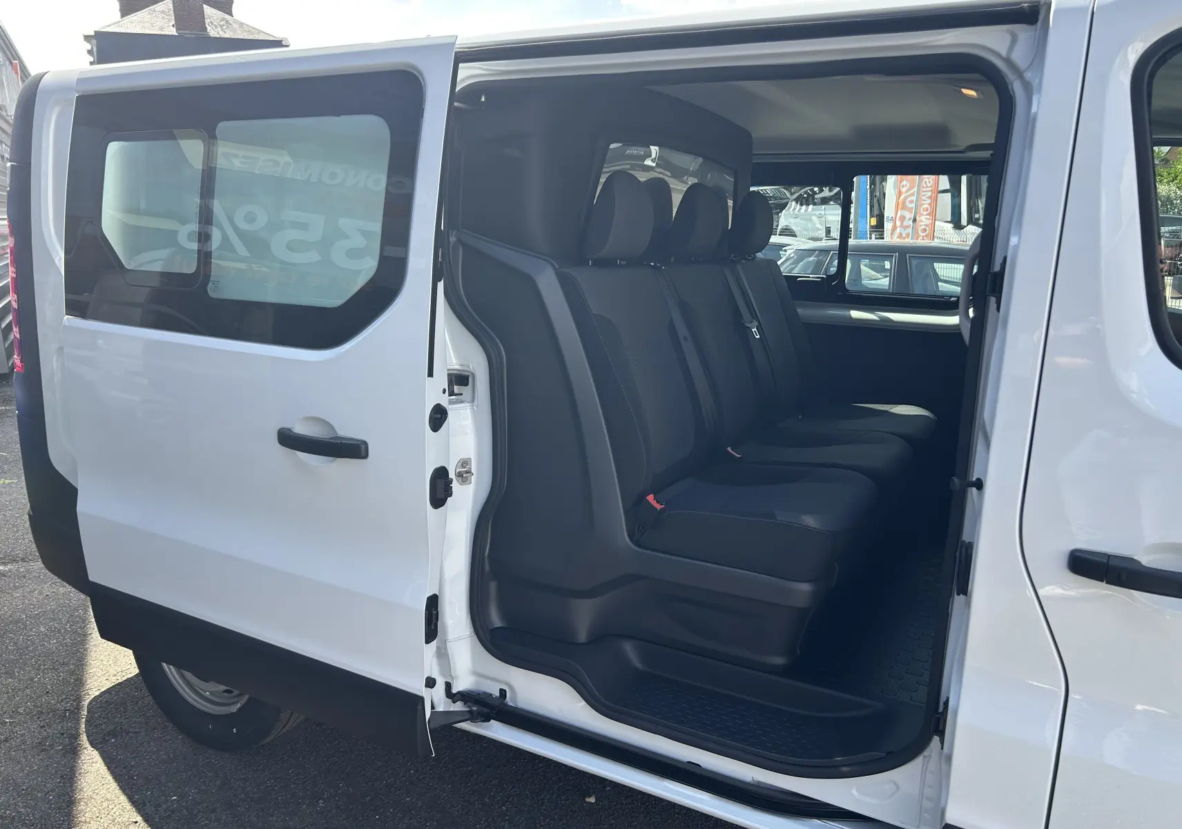 Vue latérale gauche du Renault Trafic blanc avec porte coulissante ouverte, montrant la banquette arrière 3 places en tissu noir.