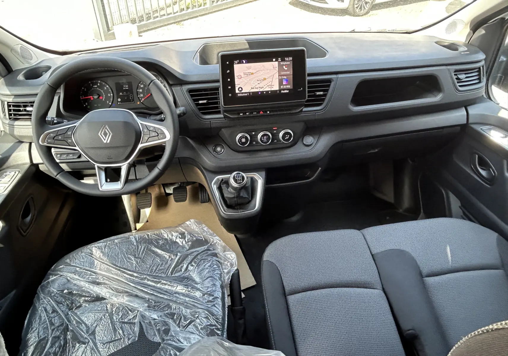 Vue intérieure avant du Renault Trafic cabine approfondie 2026, tableau de bord noir avec écran tactile et sièges tissu gris.