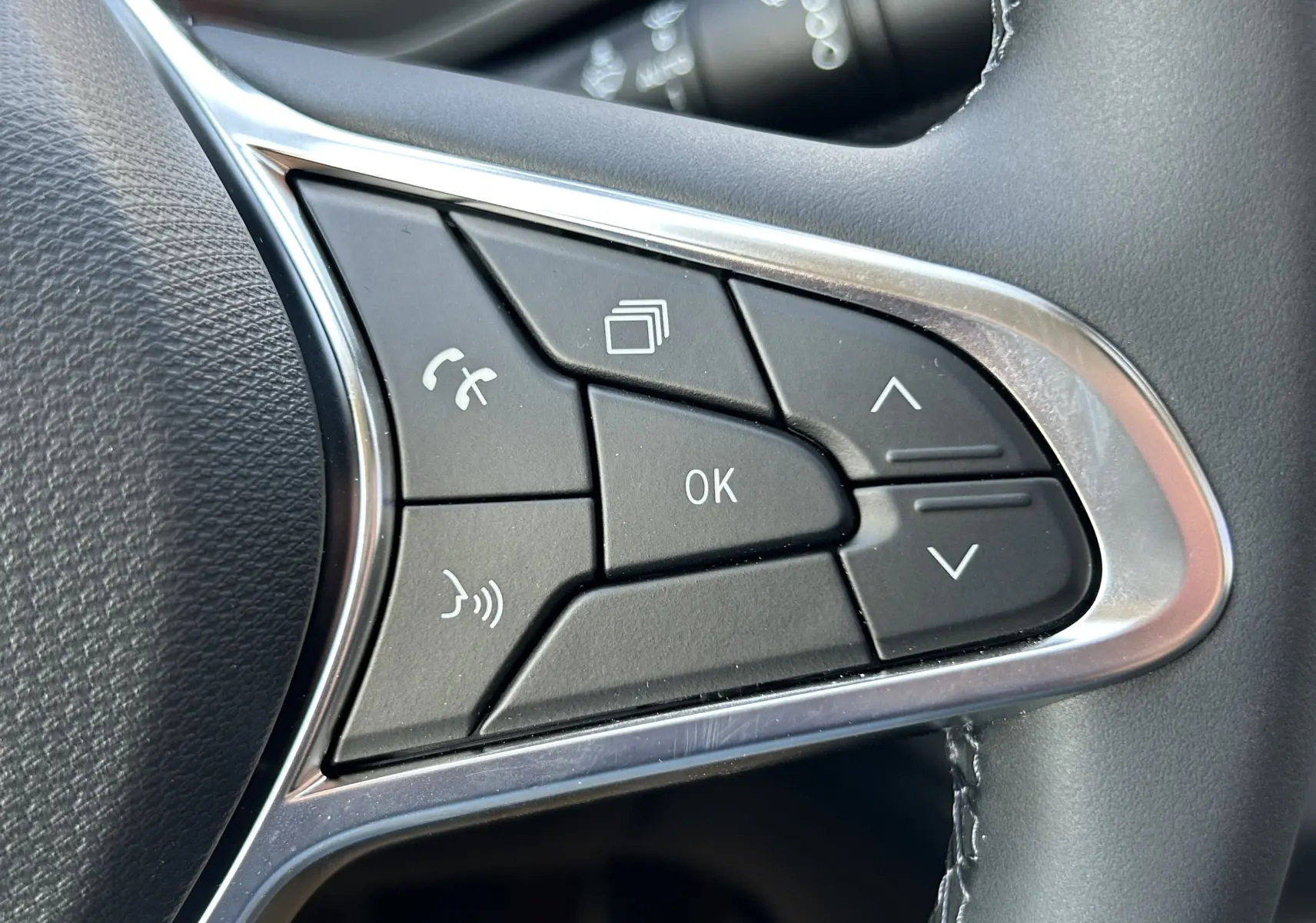 Gros plan sur les commandes multifonctions noires avec cadre chromé du volant côté gauche du Renault Trafic cabine approfondie blanc.