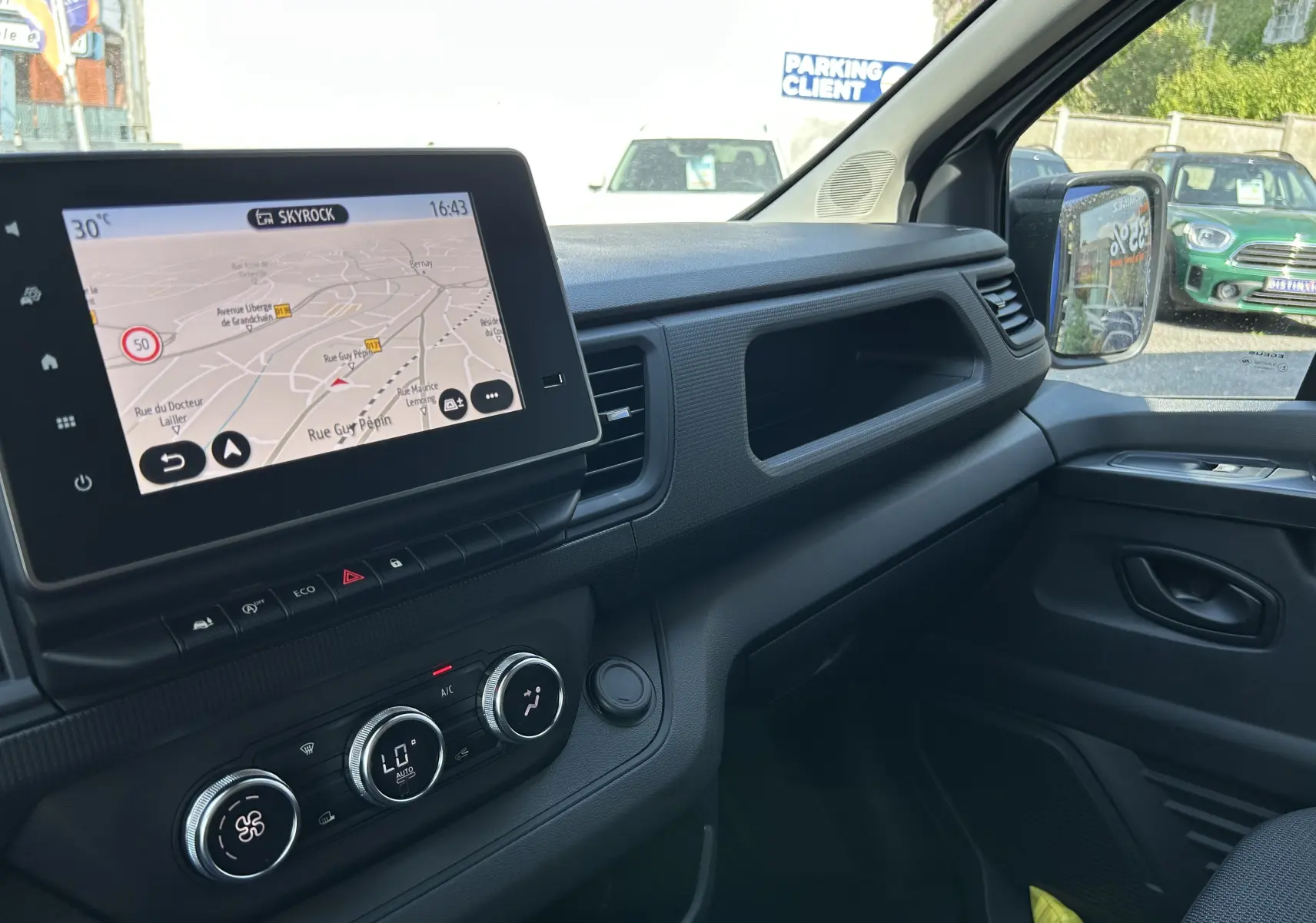 Vue intérieure côté passager du tableau de bord noir avec écran tactile et commandes de climatisation du Renault Trafic blanc.