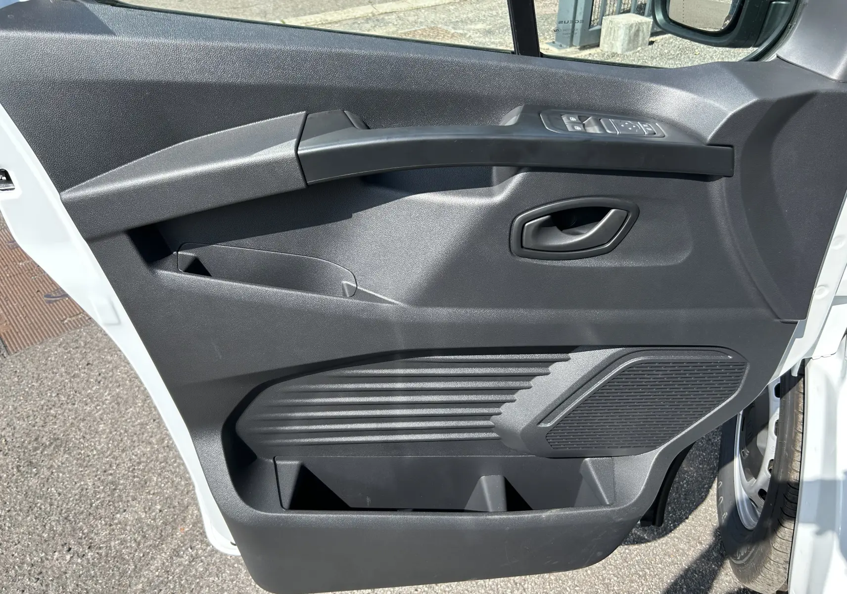Vue rapprochée de la porte avant gauche noire du Renault Trafic cabine approfondie blanc, avec commandes de vitres et poignée intégrée.