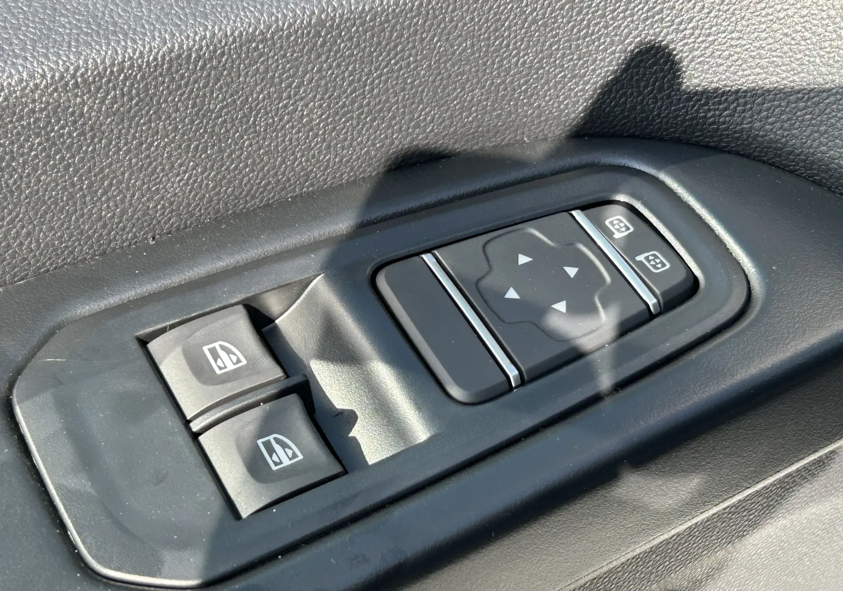 Gros plan sur les commandes de lève-vitres et réglage des rétroviseurs côté conducteur du Renault Trafic blanc.