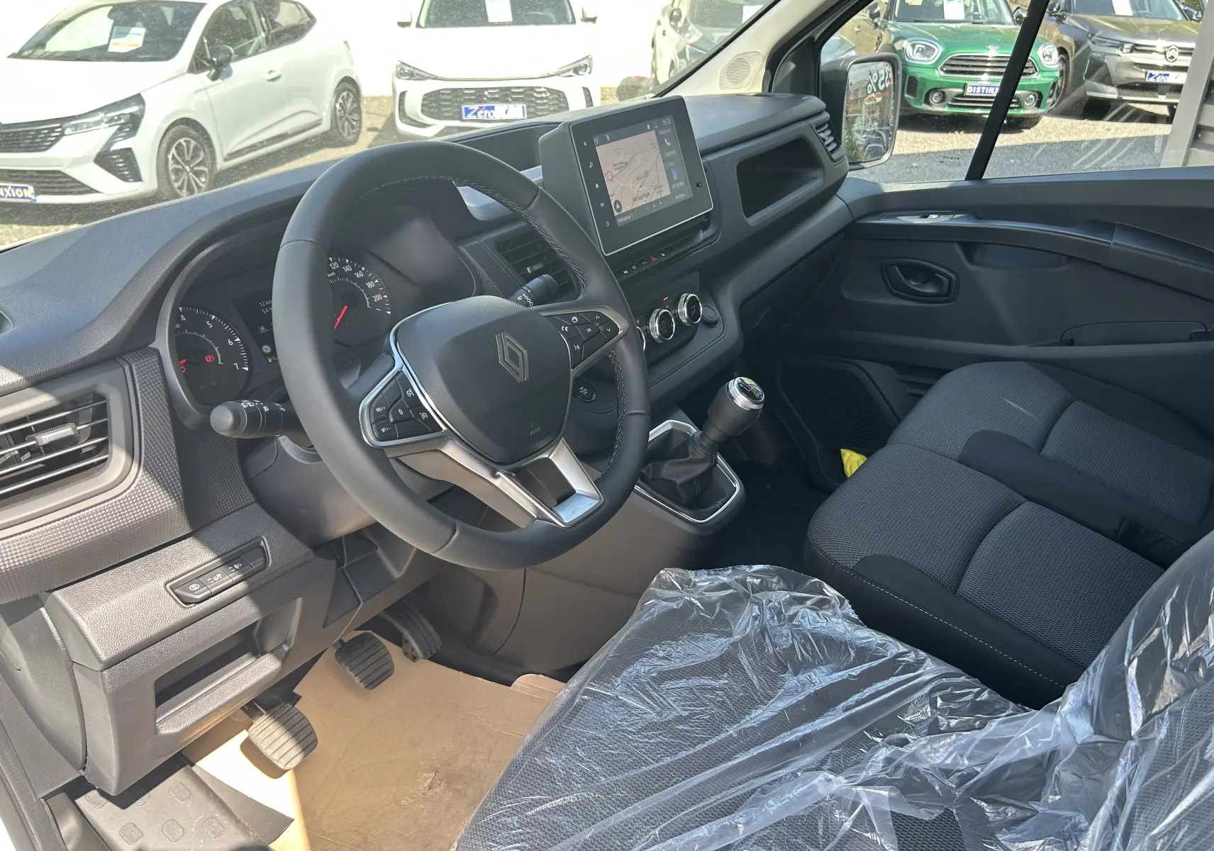 Vue intérieure côté conducteur du Renault Trafic blanc, montrant le volant multifonction, la boîte manuelle et l'écran tactile central.