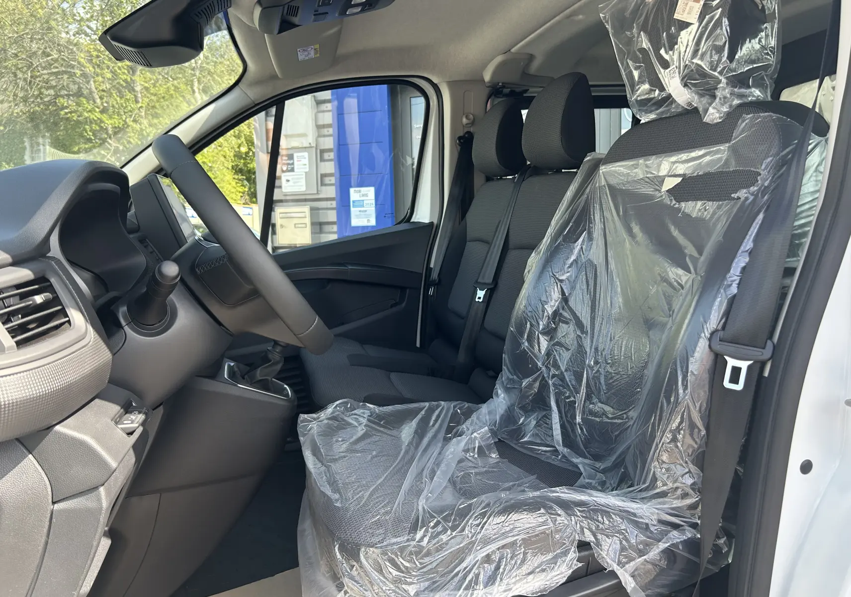 Vue intérieure côté conducteur du Renault Trafic blanc 2026, sièges avant en tissu avec protection plastique.