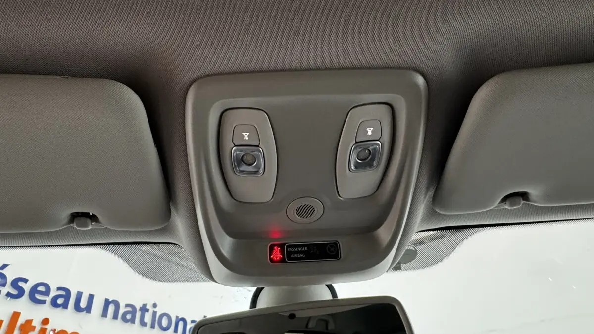 Plafonnier intérieur gris avec deux lampes de lecture et témoin airbag passager allumé dans un Renault Captur blanc.