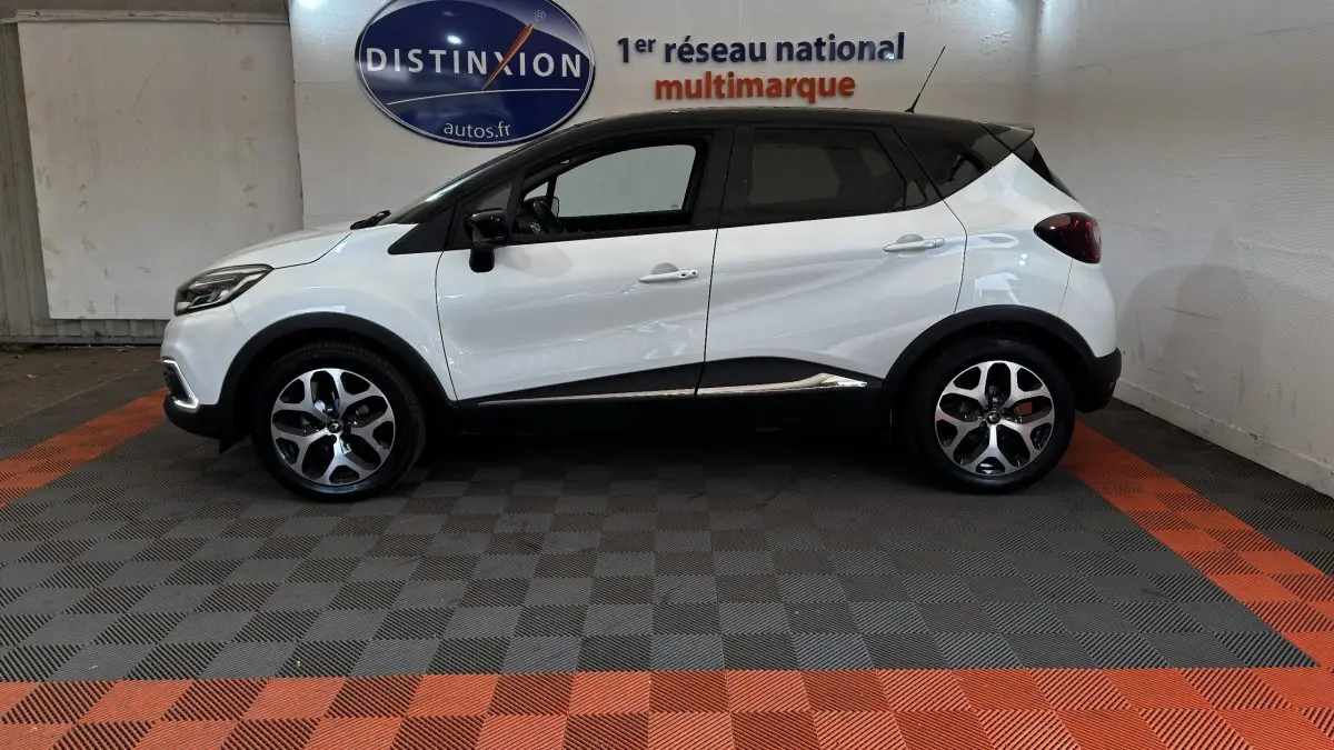 Vue de profil côté gauche d'un Renault Captur blanc avec toit noir, jantes alliage et protections noires sur les bas de caisse.