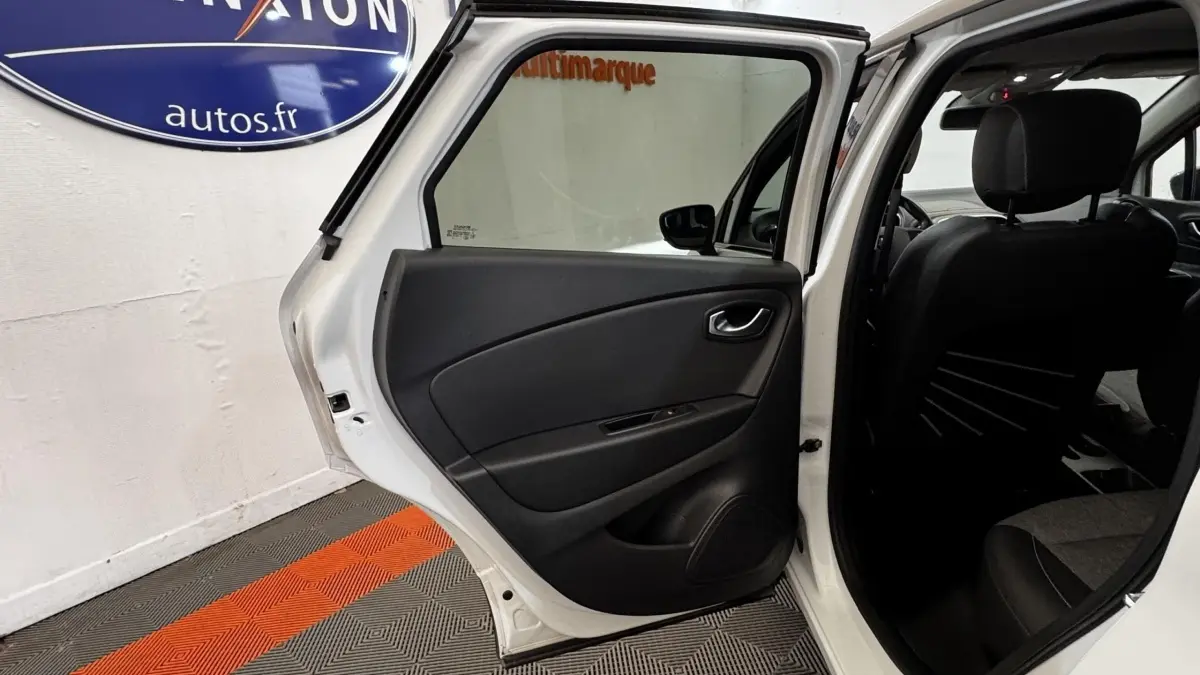 Vue intérieure de la porte arrière gauche ouverte d’un Renault Captur blanc, montrant la garniture noire et l’habitacle sombre.