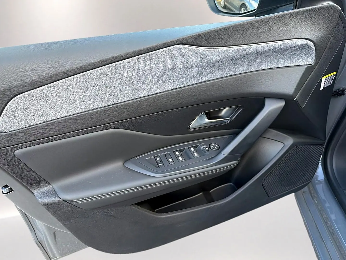 Vue rapprochée du panneau de porte avant gauche gris selenium de la Peugeot 308 1.5 BlueHDi 130 Allure EAT8 avec commandes de vitres et poignée chrome.