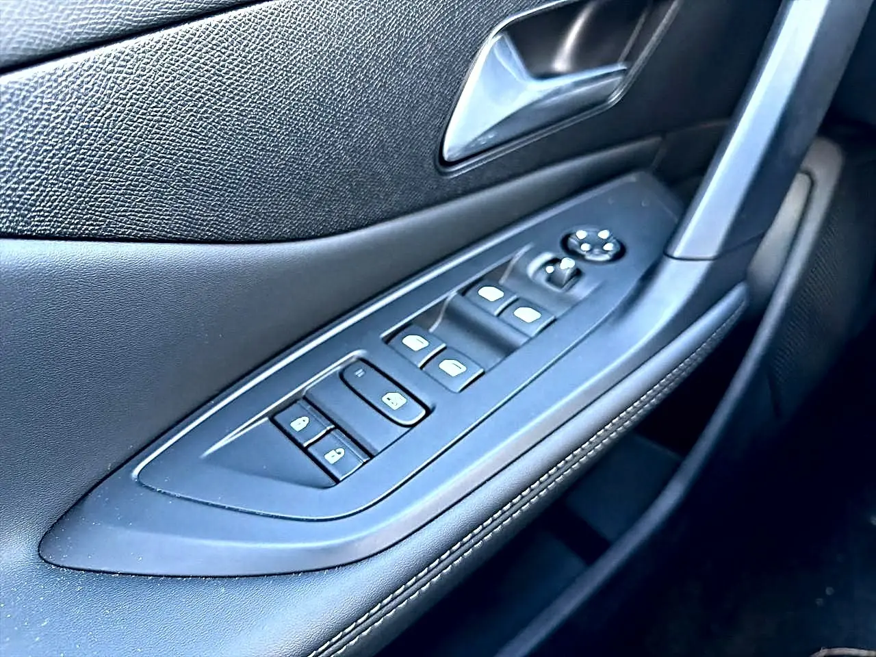 Gros plan sur la commande des vitres électriques et rétroviseurs sur la porte avant gauche en noir avec surpiqûres.