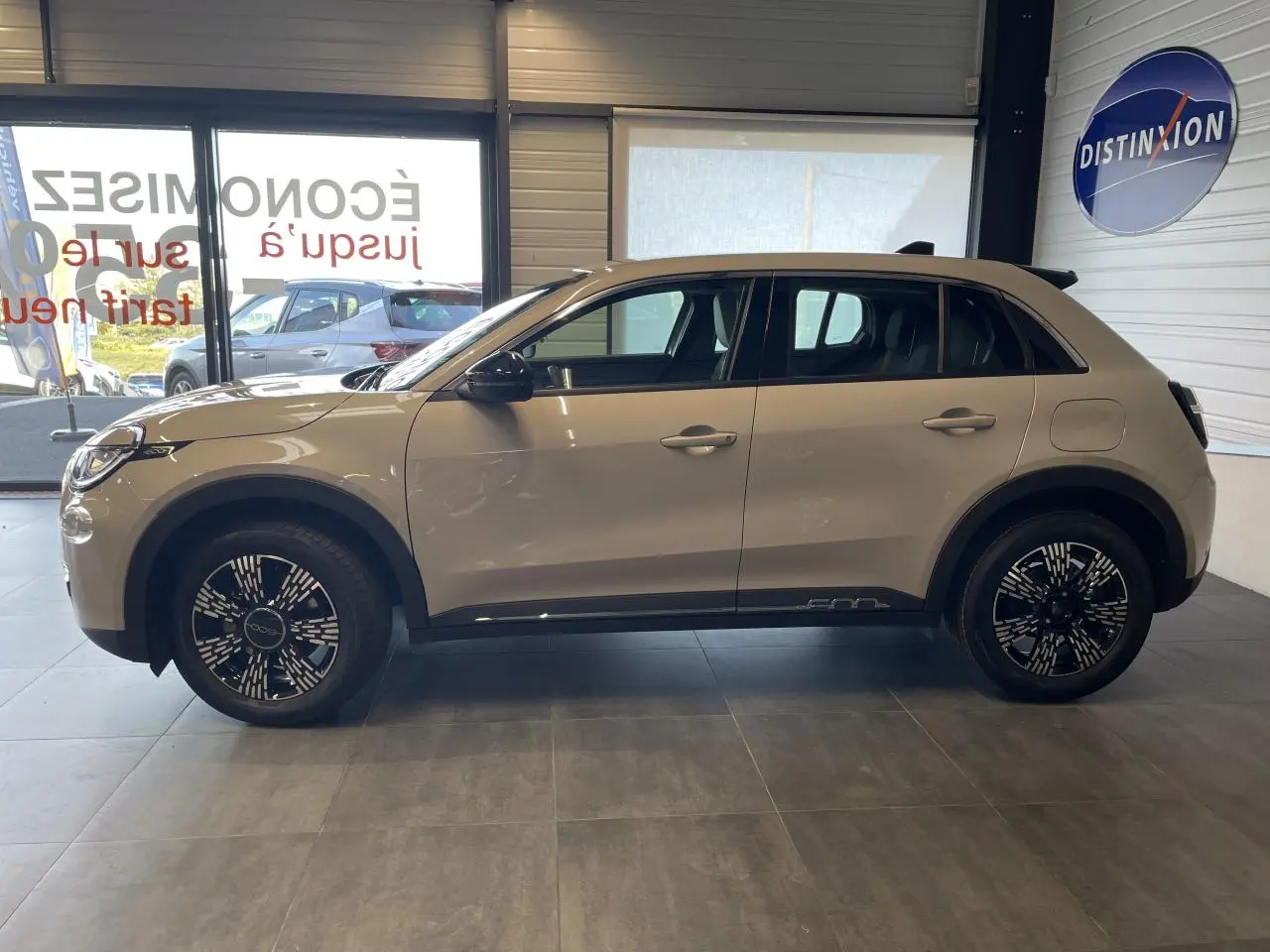 Profil côté gauche du FIAT 600 beige métallisé 2025 en intérieur, avec jantes alliage et rétroviseurs noirs brillants.