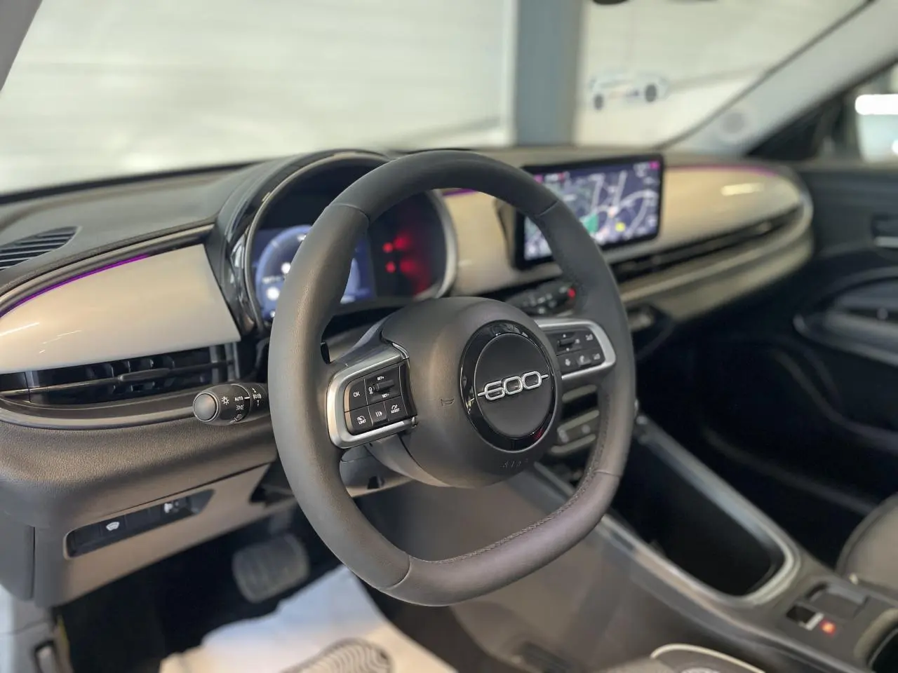 Vue intérieure du volant et tableau de bord beige métallisé du Fiat 600 1.2 Hybrid avec écran tactile central.