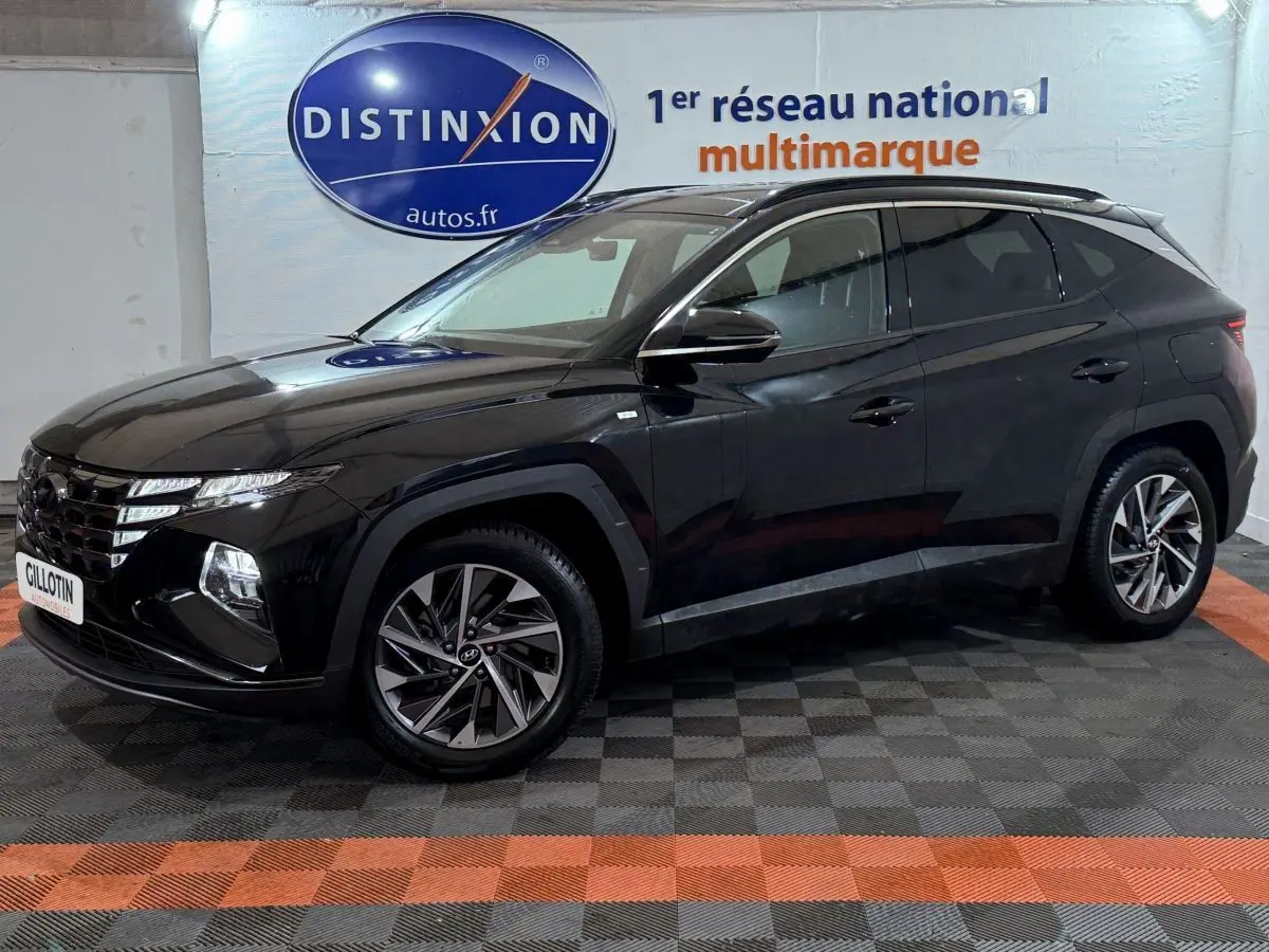 Vue 3/4 avant gauche d'un Hyundai Tucson noir brillant avec jantes alliage et vitres teintées en intérieur showroom.