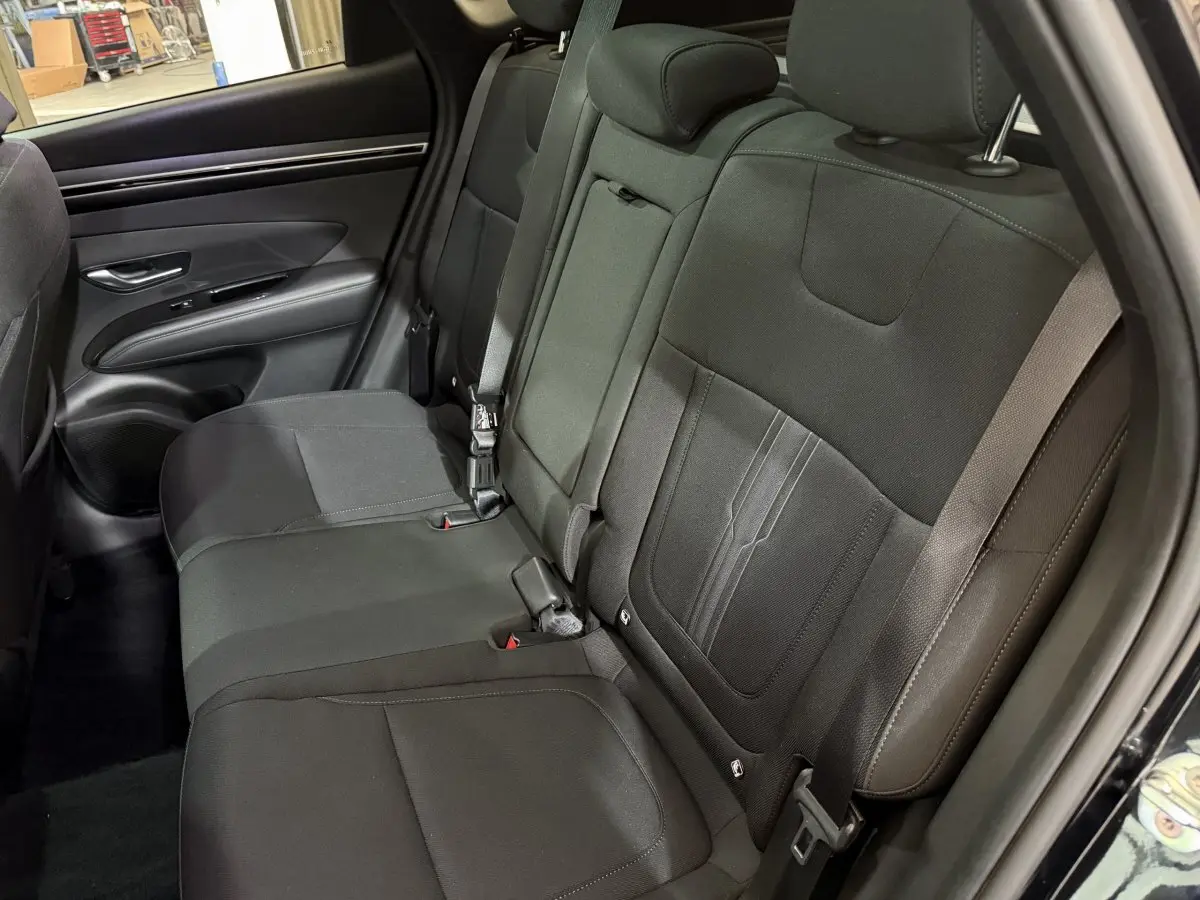 Vue intérieure du siège arrière côté gauche du Hyundai Tucson noir 2021, tissu sombre et ceintures visibles.