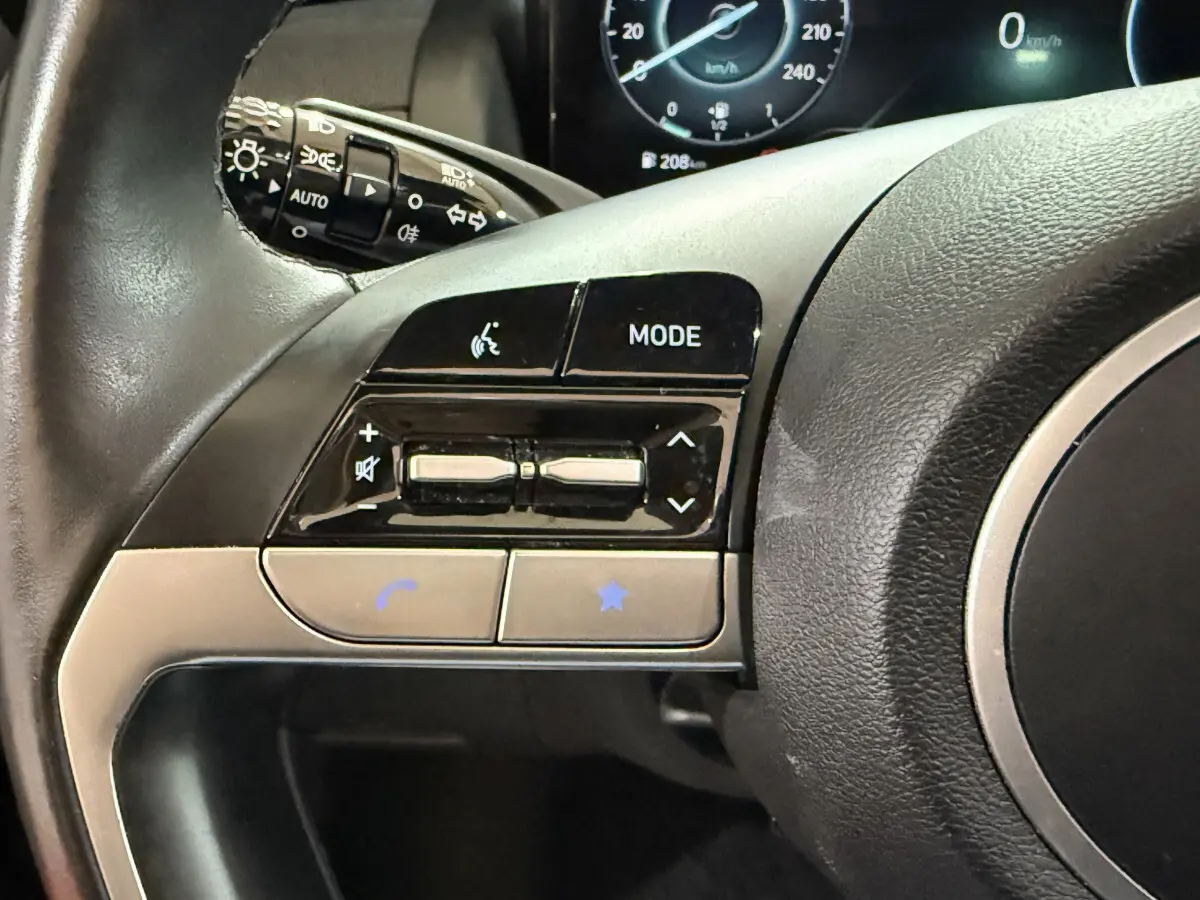 Gros plan sur les commandes du volant noir du Hyundai Tucson 2021, avec affichage digital du tableau de bord en arrière-plan.