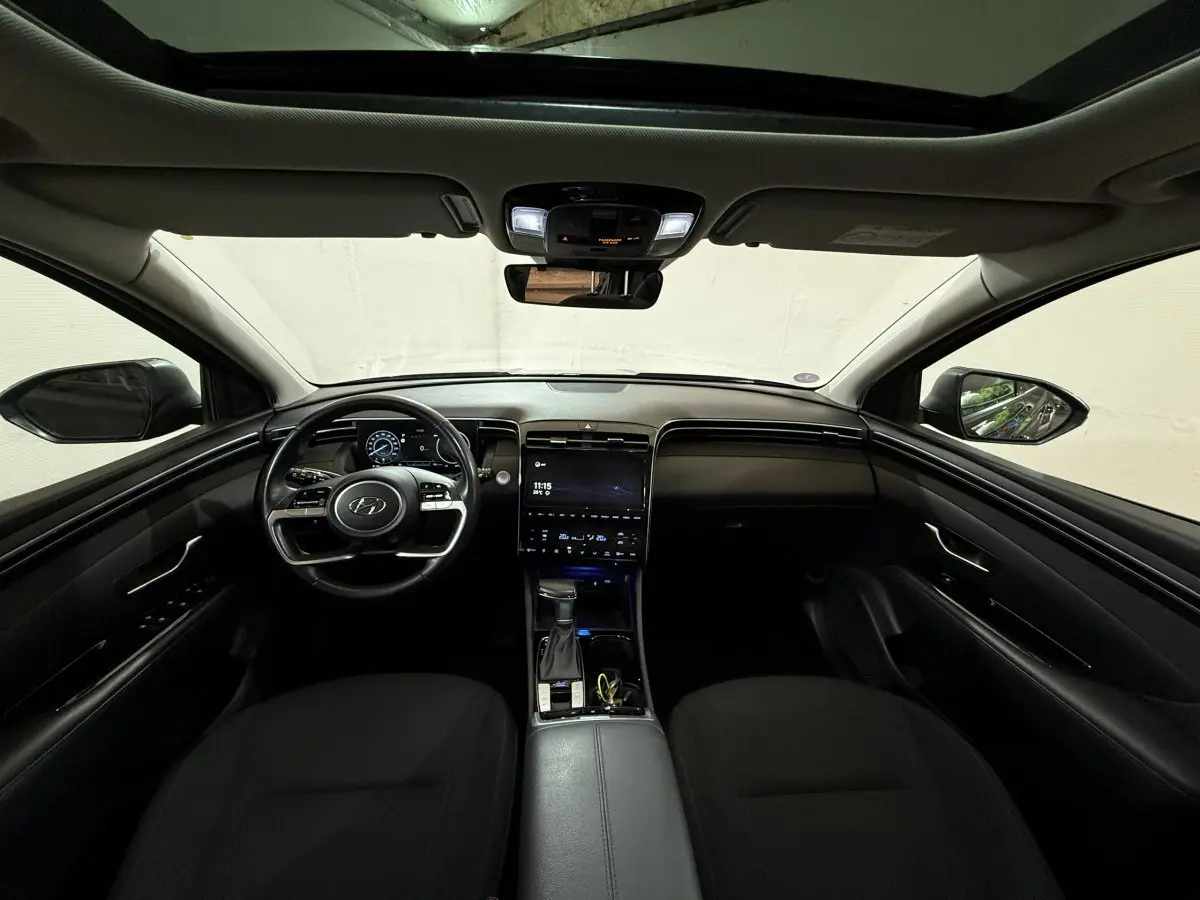 Vue intérieure avant du Hyundai Tucson noir 2021, avec tableau de bord numérique et toit ouvrant panoramique.