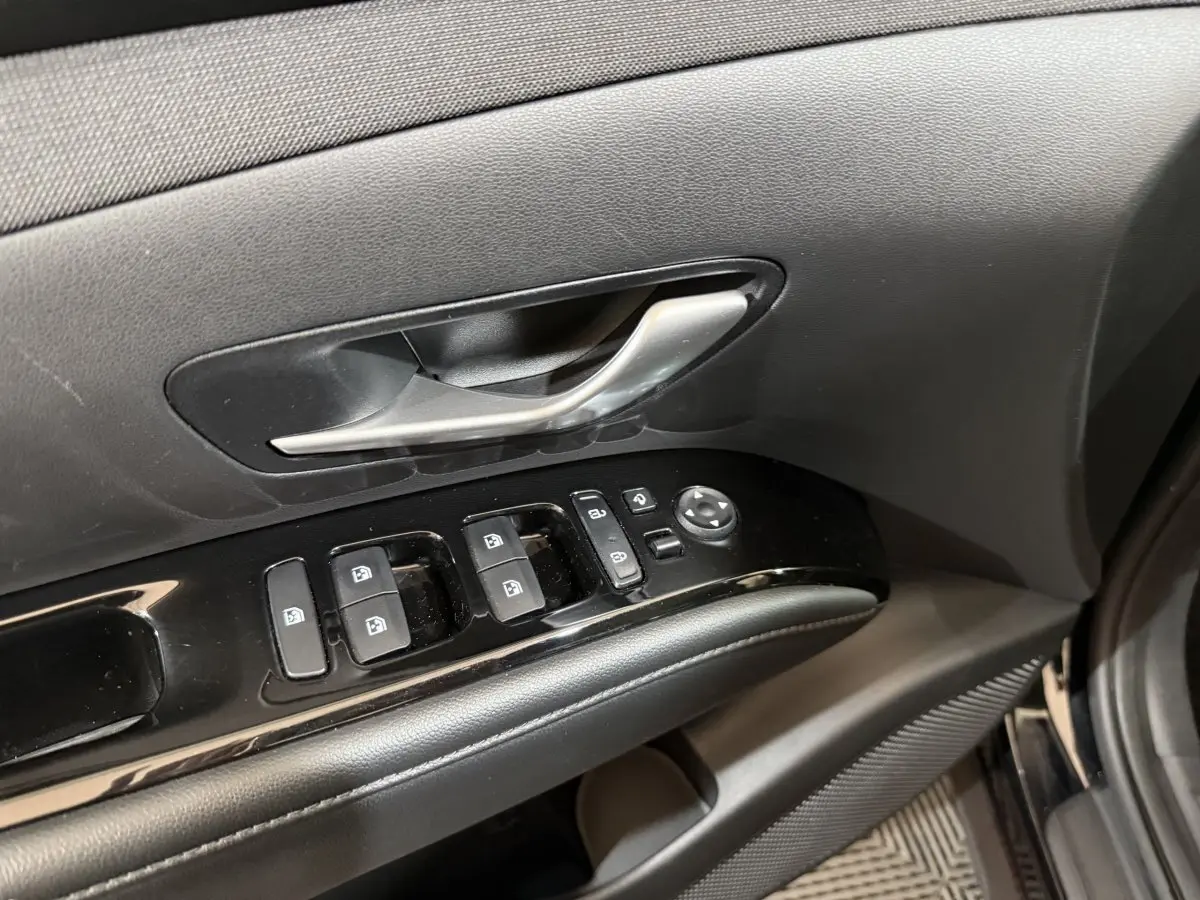 Gros plan sur la commande des vitres et la poignée intérieure côté gauche d'une Hyundai Tucson noir 2021.