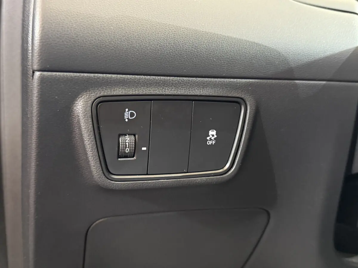 Gros plan sur les commandes de réglage des phares et de désactivation de l'antipatinage dans un Hyundai Tucson noir 2021.