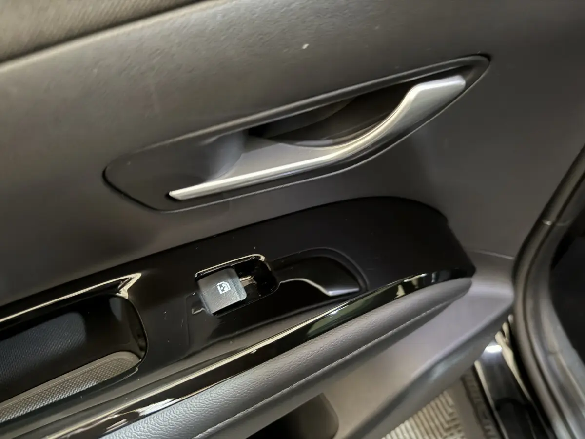 Poignée intérieure et commandes de lève-vitre côté conducteur du Hyundai Tucson noir, vue rapprochée du panneau de porte.