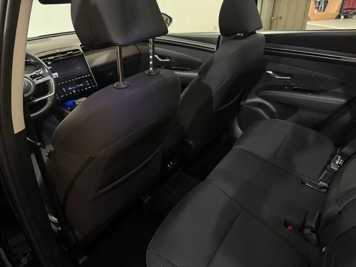 Vue intérieure arrière côté gauche du Hyundai Tucson 2021 noir, montrant les sièges arrière et le tableau de bord avant.