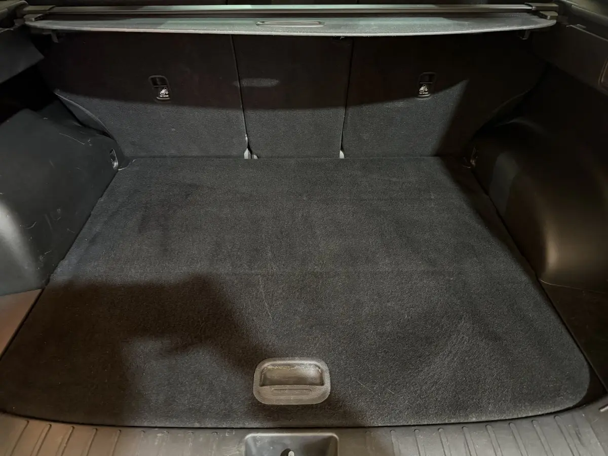 Vue intérieure du coffre noir du Hyundai Tucson 2021, version hybride 1.6 T-GDI, avec tapis de sol et sièges arrière rabattus.