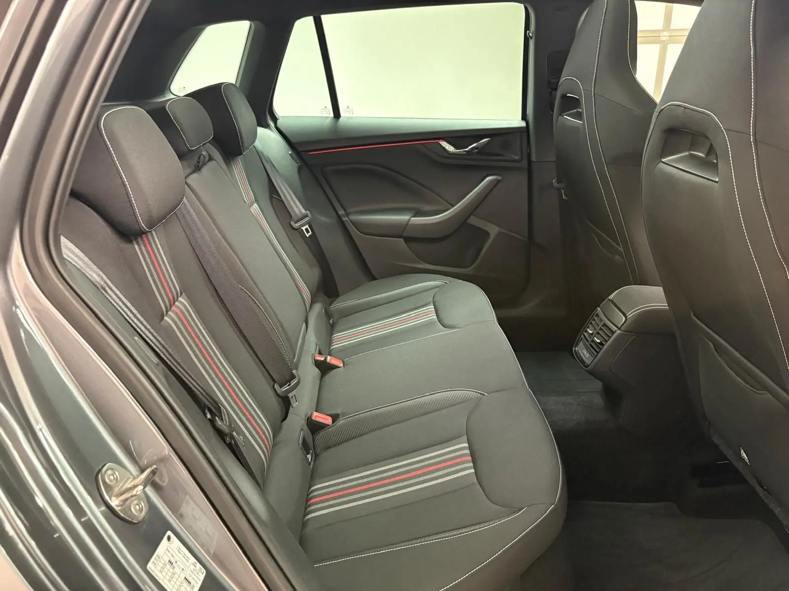 Vue intérieure arrière côté gauche du Skoda Kamiq Monte Carlo 2024 avec sièges tissu gris à bandes rouges et grises.