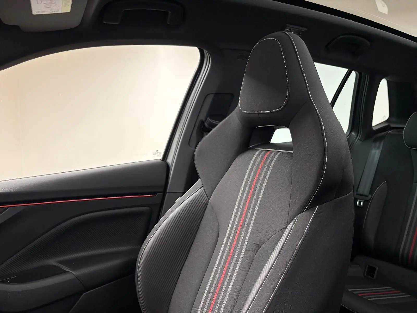 Vue intérieure côté gauche du siège avant sport noir avec surpiqûres blanches et bandes grises et rouges du Skoda Kamiq Monte Carlo 2024.