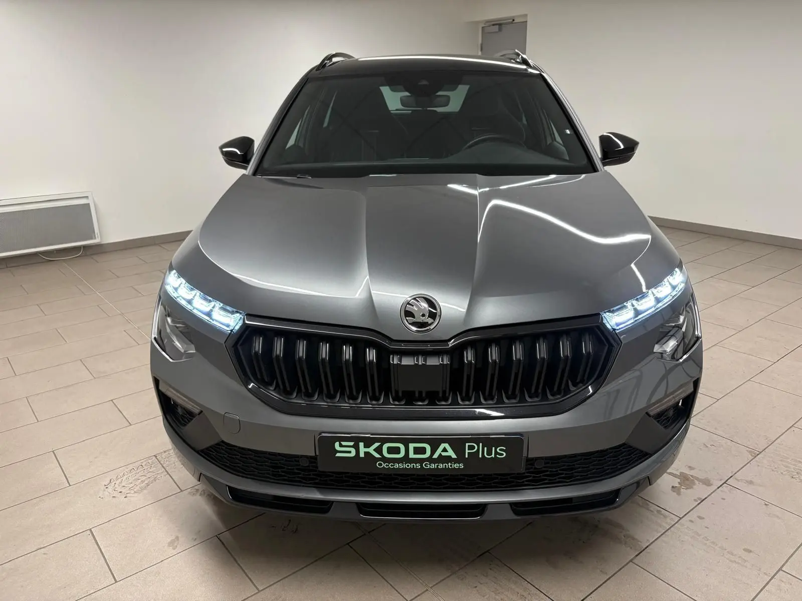 Vue frontale d'un Skoda Kamiq 1.5 TSI 150 DSG7 Monte Carlo gris graphite avec feux LED allumés en intérieur.