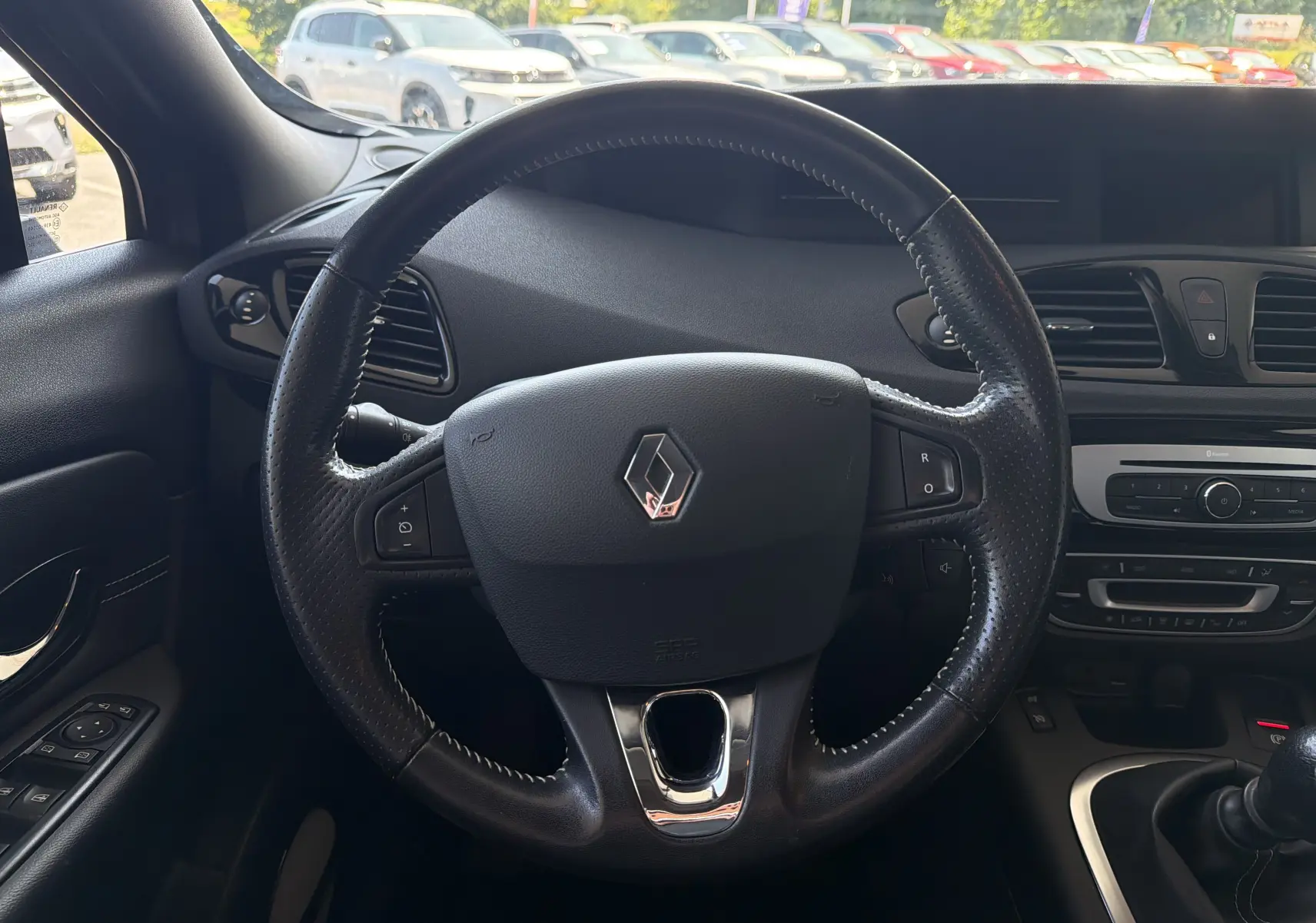 Vue centrée sur le volant en cuir noir du Renault Scenic gris Cassiopée, avec tableau de bord et commandes visibles.