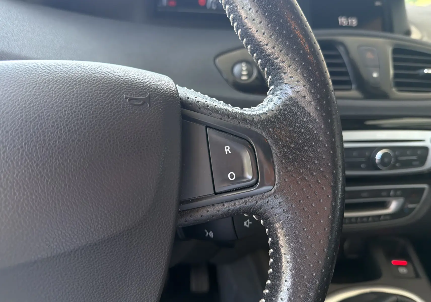 Gros plan sur le volant en cuir perforé côté droit du Renault Scénic gris, avec boutons de commande intégrés.