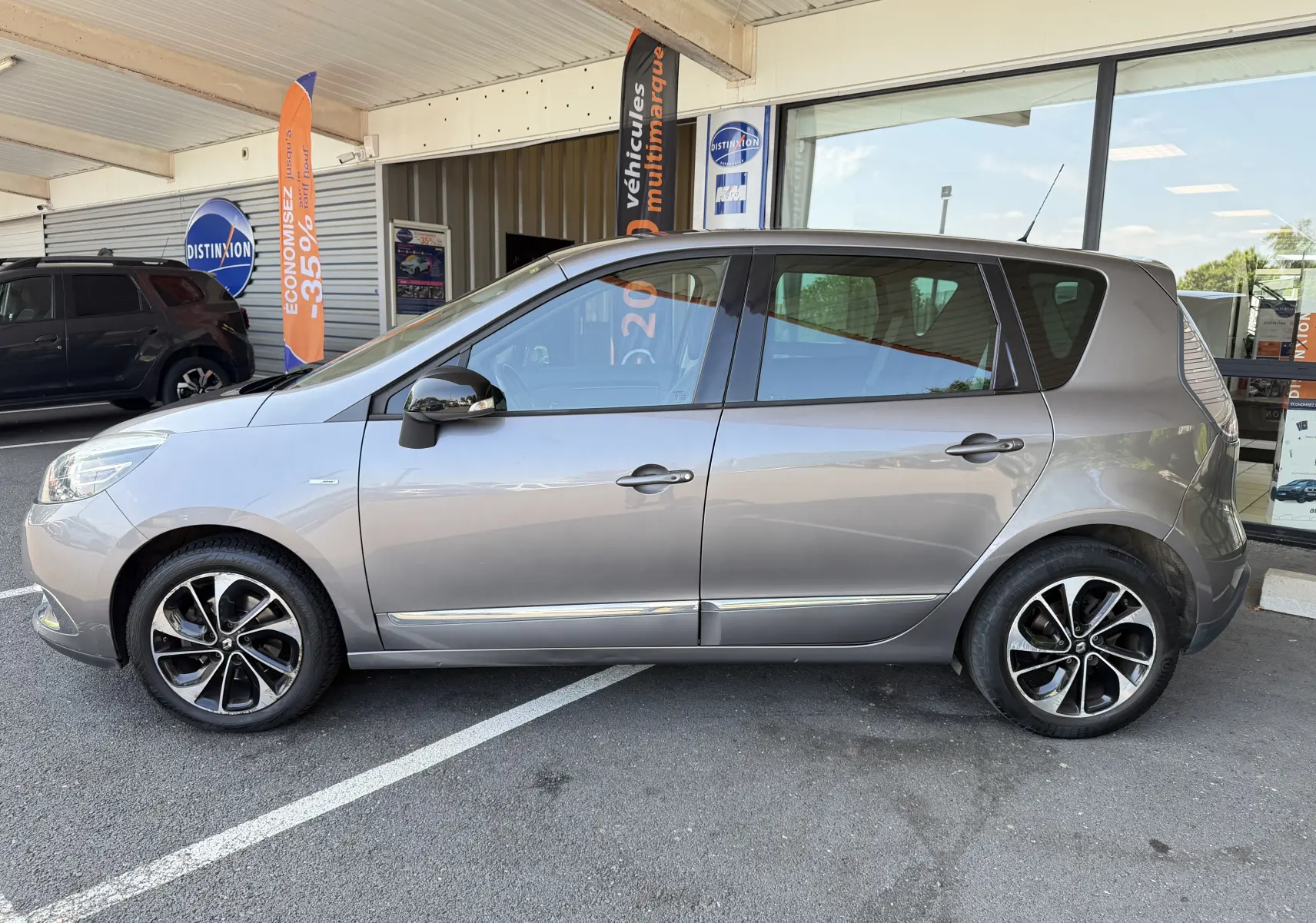 Renault Scénic gris cassiopée vue de profil côté gauche, avec jantes alliage noires et toit vitré partiel.