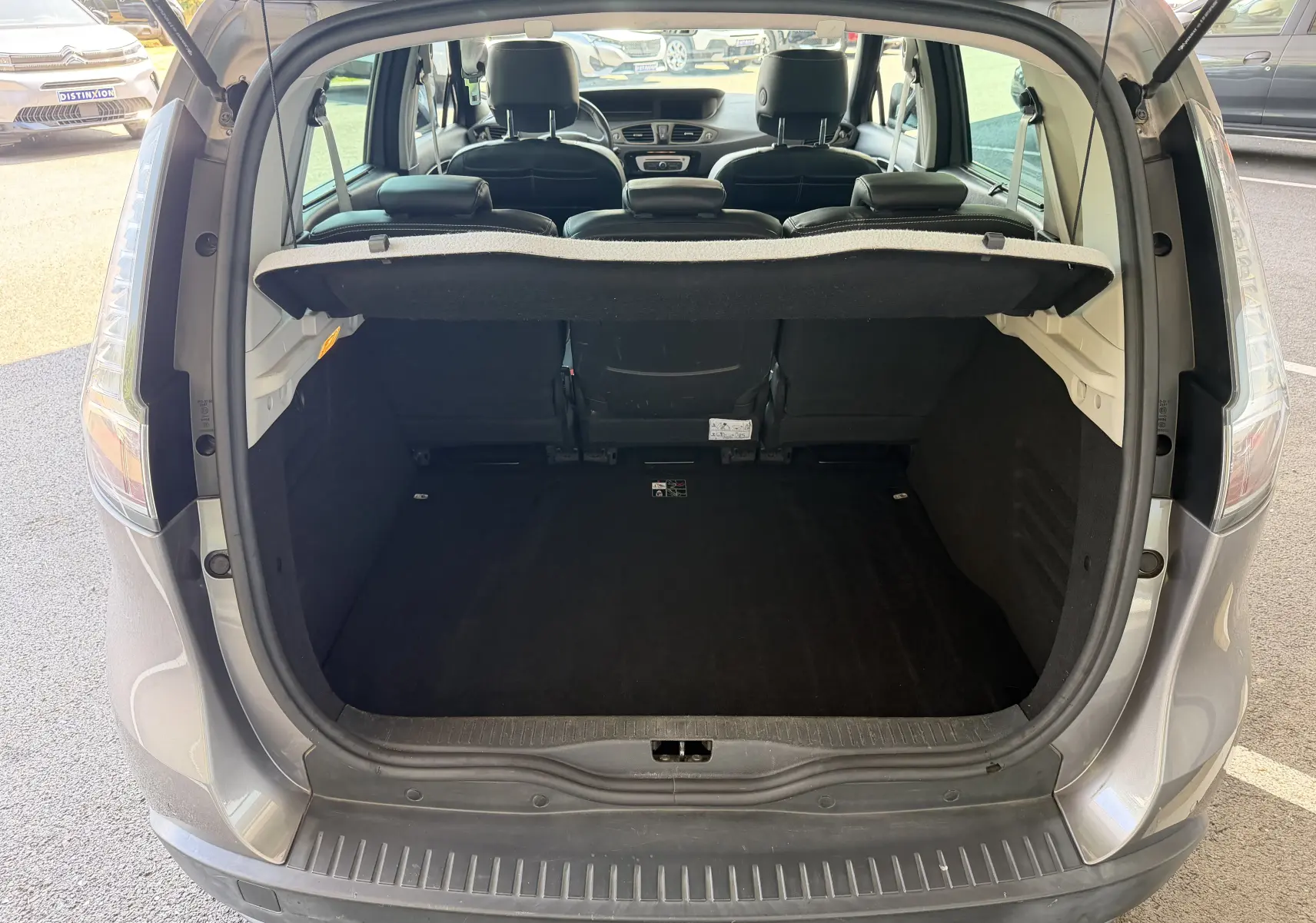 Coffre ouvert vu de l'arrière d'un Renault Scénic gris Cassiopée, montrant l'espace de chargement et l'intérieur noir.
