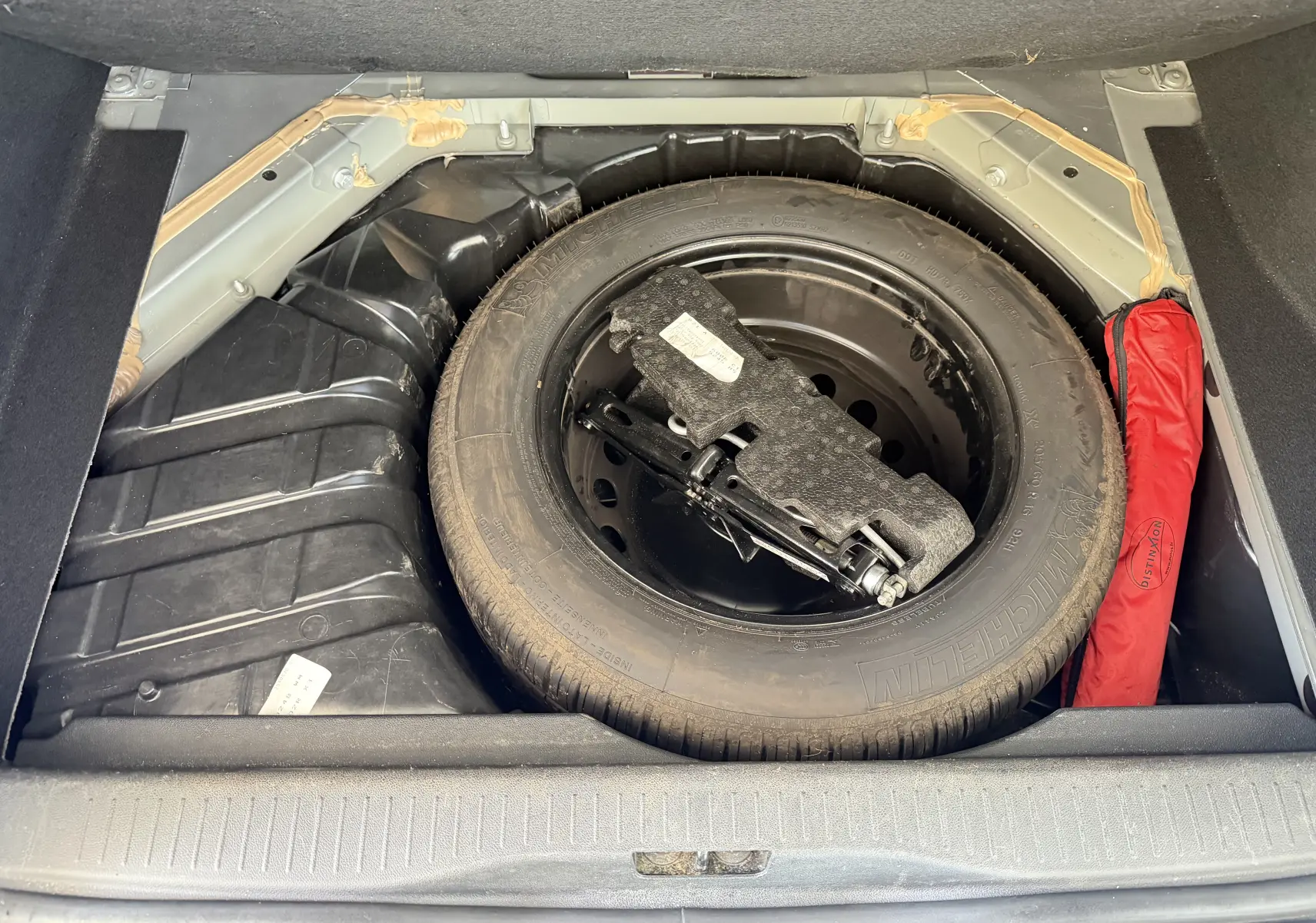 Vue plongeante sur la roue de secours noire et le cric dans le coffre d’un Renault Scenic gris Cassiopée 2015.