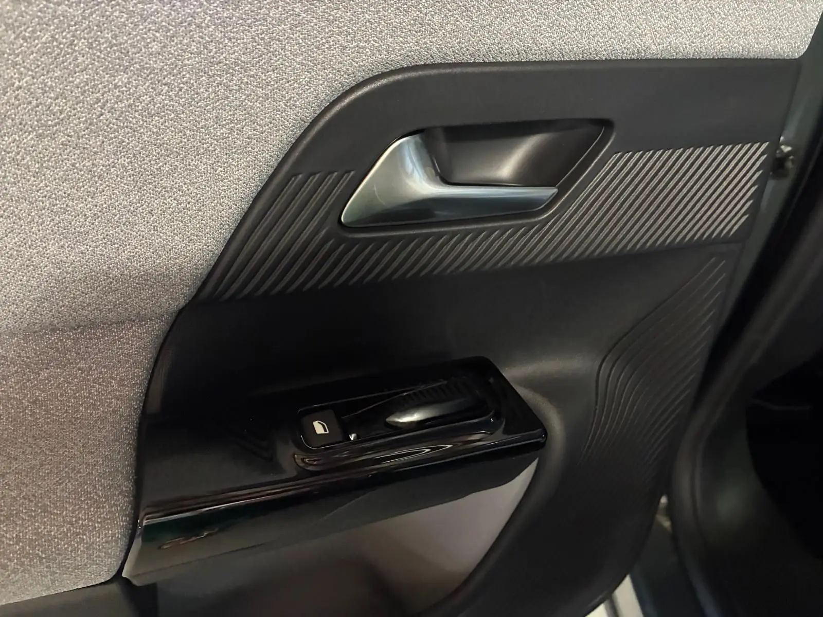 Gros plan sur la poignée intérieure et commande de lève-vitre côté gauche du Citroën C5 Aircross 2026, finition tissu gris noir.