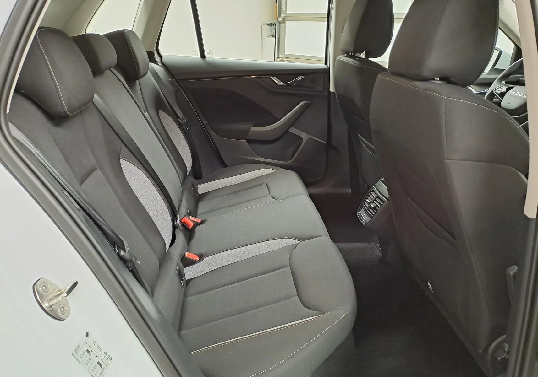 Vue intérieure côté droit des sièges arrière noirs et gris du Skoda Kamiq blanc Lune 2025 avec porte ouverte.