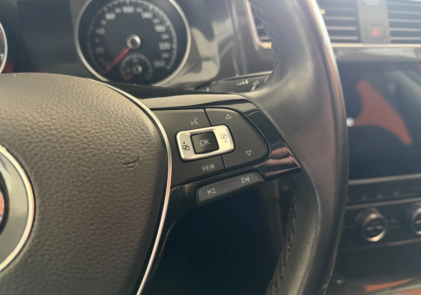Gros plan sur le volant noir de la Volkswagen Golf TSI 130 Confortline 2019, avec commandes multifonctions et tableau de bord flou.