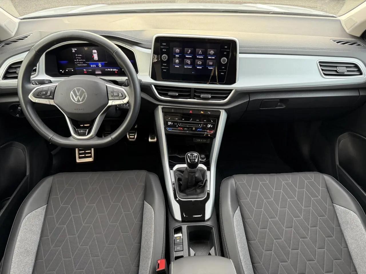 Intérieur du Volkswagen T-Roc 2025 vu de face, tableau de bord moderne avec écran tactile et volant cuir multifonction.