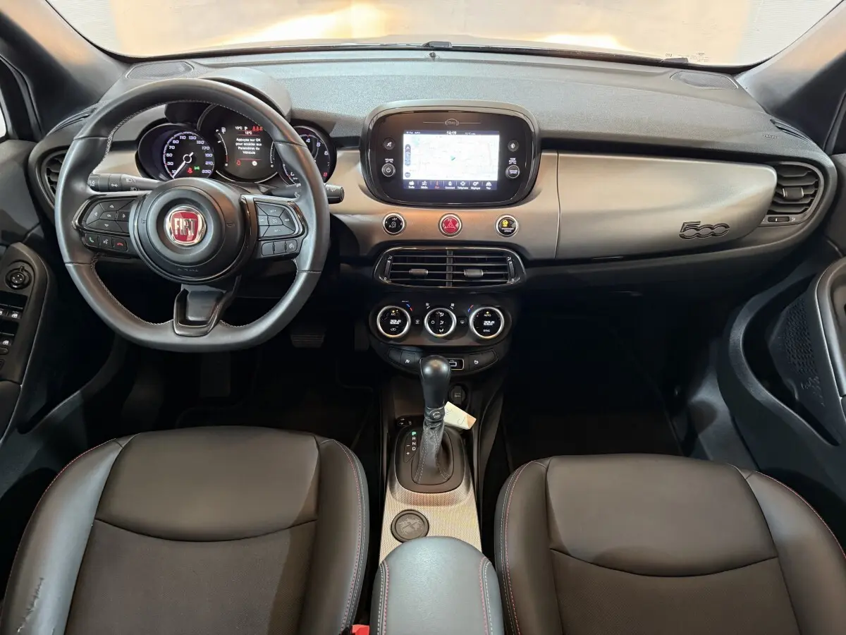 Vue intérieure avant de la Fiat 500X noire, tableau de bord avec écran tactile central et volant multifonctions en cuir.